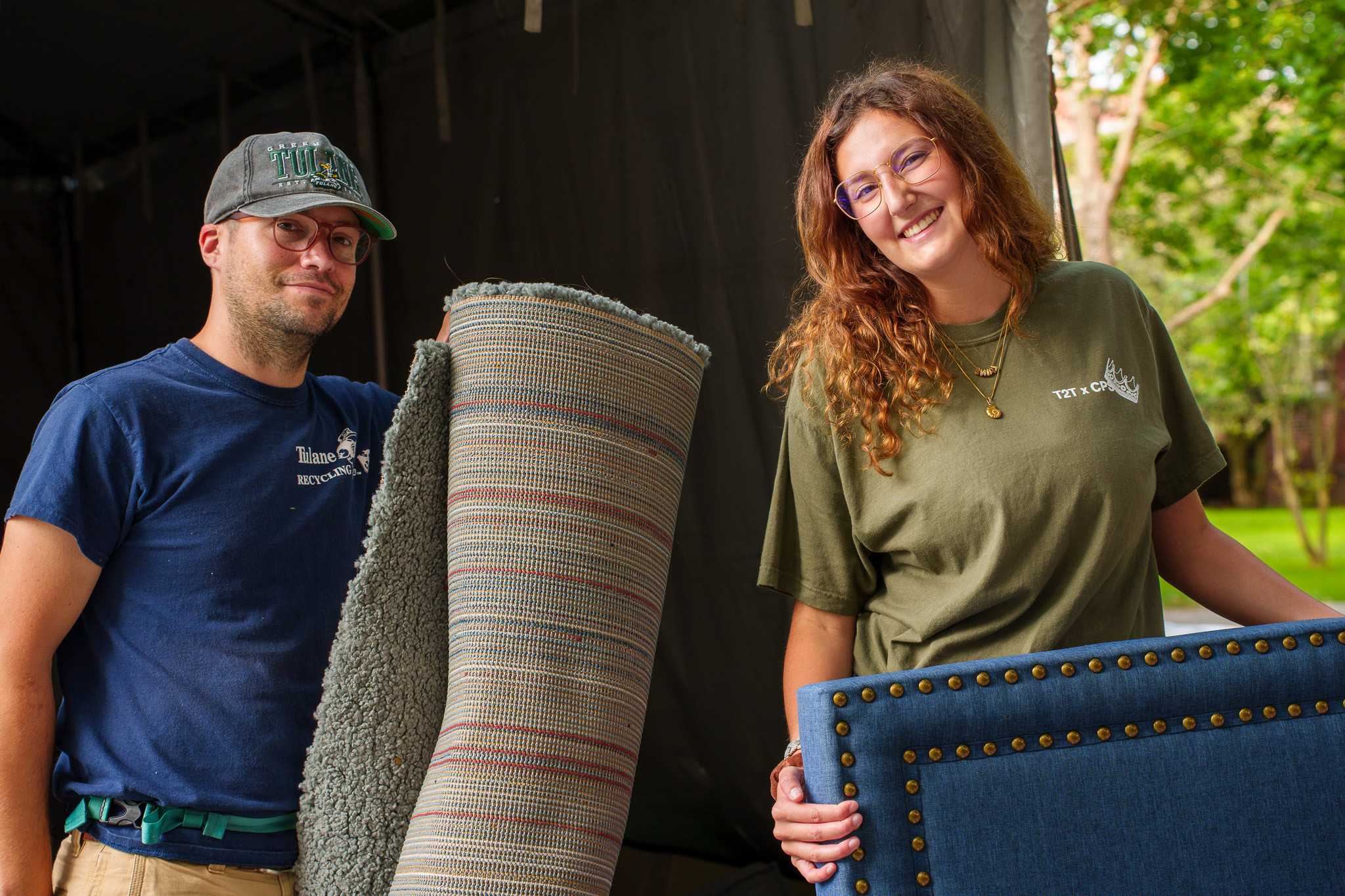 A photo of two people moving a rush and headboard for a bed.