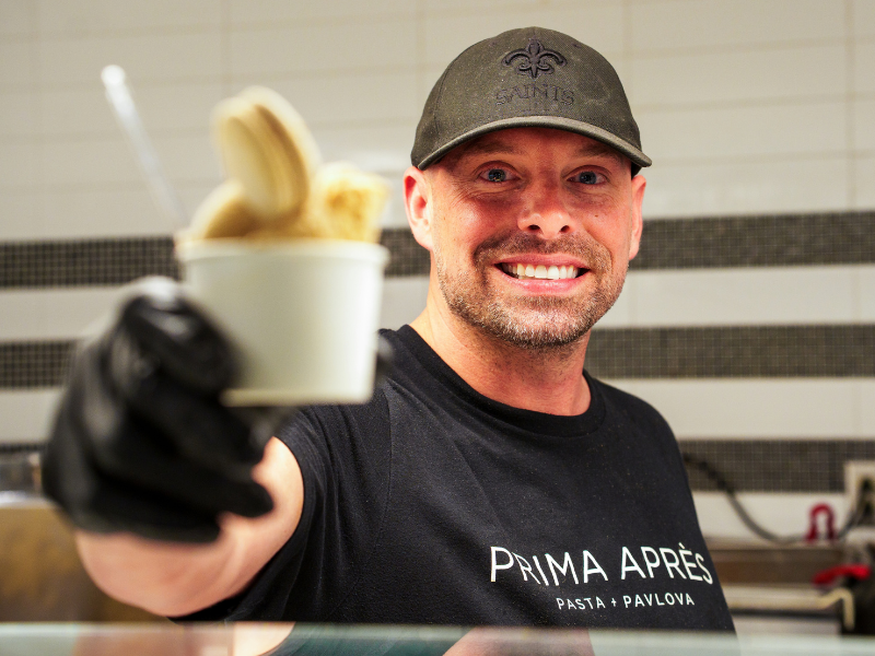 A person smiling and holding up a cup of gelato.
